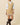 A tan Women’s Cotton Blend Cable Dress Camel featuring a V-neck and red and white striped trim, worn over a white collared shirt with tall dark boots.