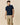 A man wearing a Rowing Blazers x Winnie-the-Pooh Men’s Short Sleeve Eeyore Pique Polo Navy, featuring a small light blue embroidered Eeyore icon on the chest.