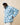 A person wears a light blue Sheep Sherpa Jacket by Warm & Wonderful featuring a repeating white sheep pattern, paired with a baseball cap.