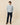 A man wears a Rowing Blazers Men’s Casual Linen Band Collar Shirt Blue Stripe with dark trousers and brown deck shoes.
