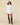 A woman wearing a Rowing Blazers Women’s Button Down Pleated Shirt Dress White in 100% cotton with a pleated skirt and tall dark brown leather boots.