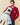 A man wearing a burgundy Men’s Cotton Cable Sheep Sweater by Warm & Wonderful holds a decorative sheep figure wearing a light blue beret and matching scarf.