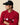 A man with his arms crossed wears a red Men’s Cotton Cable Sheep Sweater Burgundy with a row of sheep and a matching black baseball cap featuring a sheep icon.