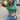 A woman wears a Men’s Cotton Patch T-Shirt Green, featuring an embroidered chest patch, with blue jeans and a plaid fabric belt while standing on a city sidewalk.