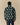 A person seen from behind wears a Warm & Wonderful Sheep Sherpa Jacket Green, featuring a green sherpa fleece with an all-over white and black sheep pattern.