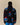Someone wearing the Paddington Sherpa Jacket Navy by Rowing Blazers x Paddington™, seen from the back against a plain beige background. The fuzzy navy fleece features colorful cartoon bears in red hats and blue coats.