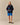 A person wears a Rowing Blazers x Paddington™ Paddington Sherpa Jacket Navy with blue shorts and black shoes, standing against a plain beige background.