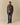 A man stands against a beige background wearing a brown sweater with a cartoon figure, blue jeans, brown shoes, and a Rowing Blazers Donegal Fair Isle Scarf Green.