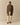 A man in a brown checkered coat, Donegal Fair Isle Crew Sweater Green by Rowing Blazers, light pink shirt, cream pants, and brown shoes stands facing forward against a beige background.