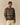 A person wears the Donegal Fair Isle Crew Sweater Green by Rowing Blazers over a light pink collared shirt and cream pants, standing against a plain beige background.