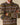 A person in a pink collared shirt under the Rowing Blazers Donegal Fair Isle Crew Sweater Green, a 100% wool sweater with green, blue, pink, and white geometric designs and crossed arms.