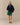 A person wears a navy blue Rowing Blazers Clark Sherpa Navy pullover with purple trim, dark green athletic shorts, and tan suede shoes.