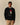 A model wears a black Paddington Tuxedo Wool Sweater featuring an intarsia knit graphic of a bear in a tuxedo and a red hat.