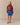 A person wears a red Jamie Cropped Button Snap Sheep Sherpa, blue athletic shorts, and tan slip-on shoes.