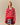 A woman wears the Warm & Wonderful Diana Edition Cotton Linen V-Neck Sheep Sweater Red over a blue collared shirt and plaid skirt, standing against a plain beige background.