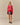 A woman stands against a plain background wearing the Warm & Wonderful Diana Edition Cotton Linen V-Neck Sheep Sweater Red over a blue collared shirt, paired with a plaid skirt and black Mary Jane shoes.