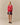 A woman wears the Warm & Wonderful Diana Edition Cotton Linen V-Neck Sheep Sweater Red with a blue collared shirt, plaid skirt, and black shoes against a plain beige background.