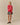 A model wears a Warm & Wonderful Wool Diana Edition Sheep Sweater Diana Red over a white collared shirt, paired with a grey gingham pleated skirt and black Mary Jane shoes.