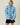 A person wears a blue Warm & Wonderful Sheep Sherpa Jacket featuring an all-over white sheep pattern, a zip-up front, and black trim reminiscent of the iconic black sheep sweater.